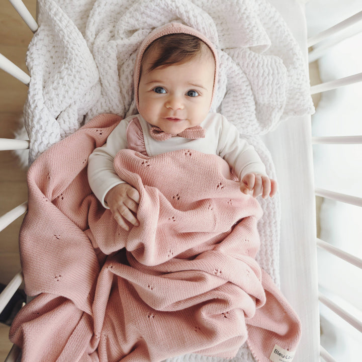 baby in bassinet covered in powder pink organic cotton knit blulala swaddling and receiving blanket 