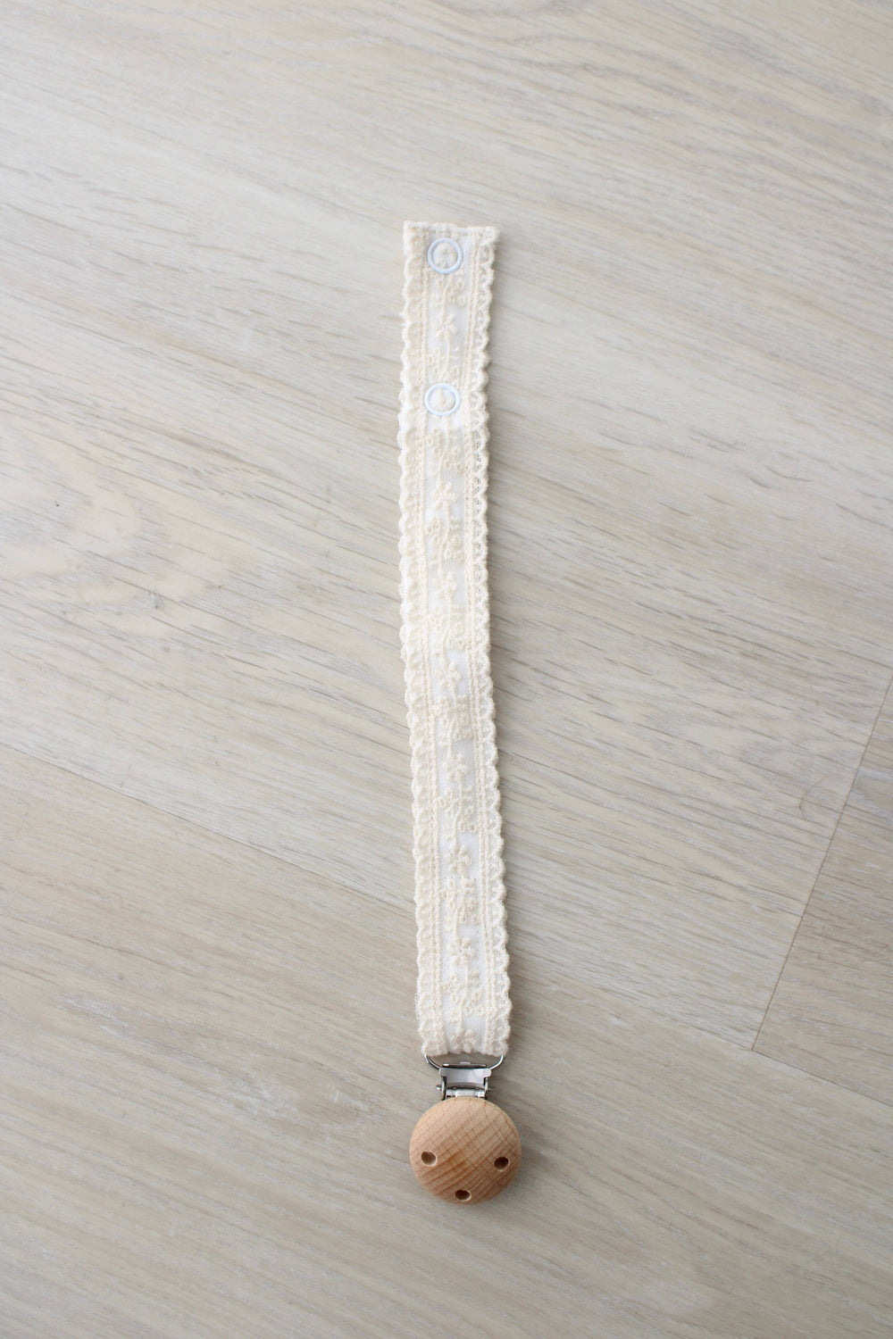 Ivory floral lace pacifier clip laid flat with a wooden clasp, Little Threads binky holder for baby girls on the go