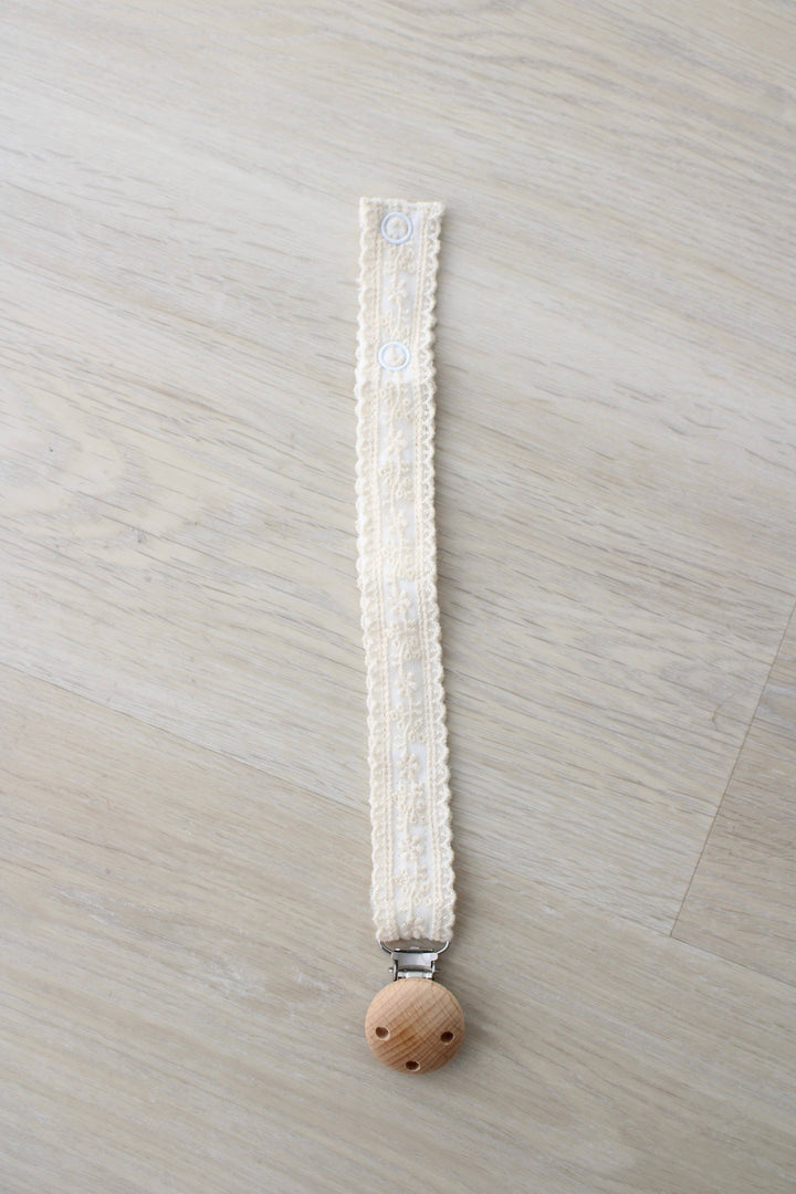 Ivory floral lace pacifier clip laid flat with a wooden clasp, Little Threads binky holder for baby girls on the go