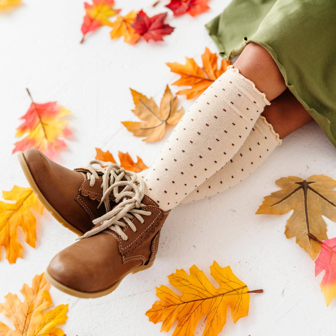 Autumn leaves surround these Little Stocking Co. Dottie Knee Socks in Vanilla, worn with lace-up boots