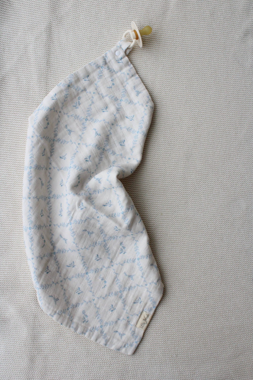 Blue lattice lovey by Little Threads rolled on its side with pacifier clip attached