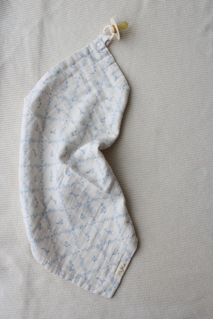 Blue lattice lovey by Little Threads rolled on its side with pacifier clip attached