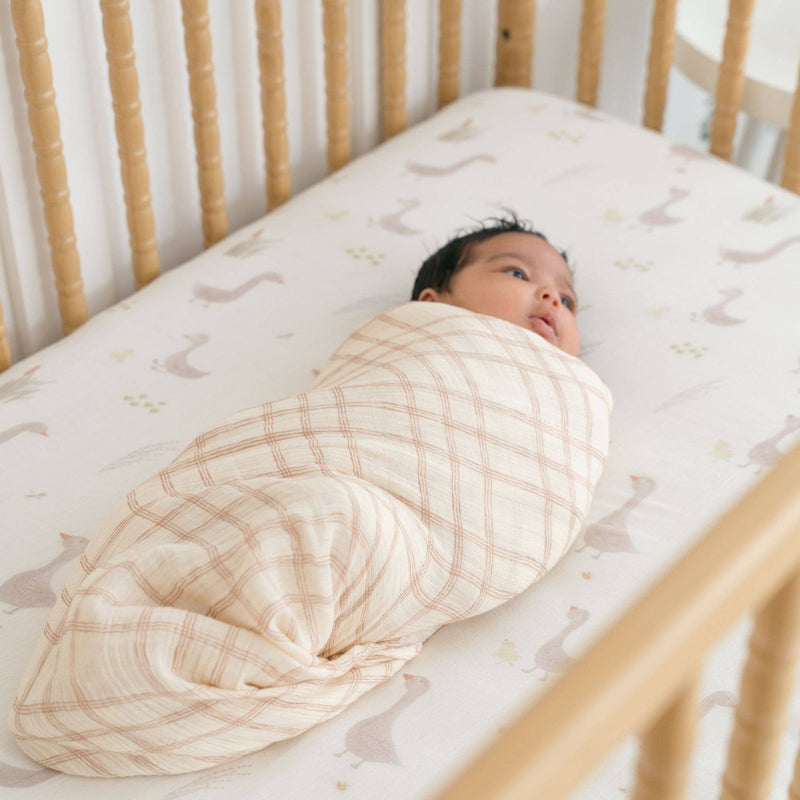 baby laying on crane baby goose sheets wrapped in farmhouse plaid baby swaddle 
