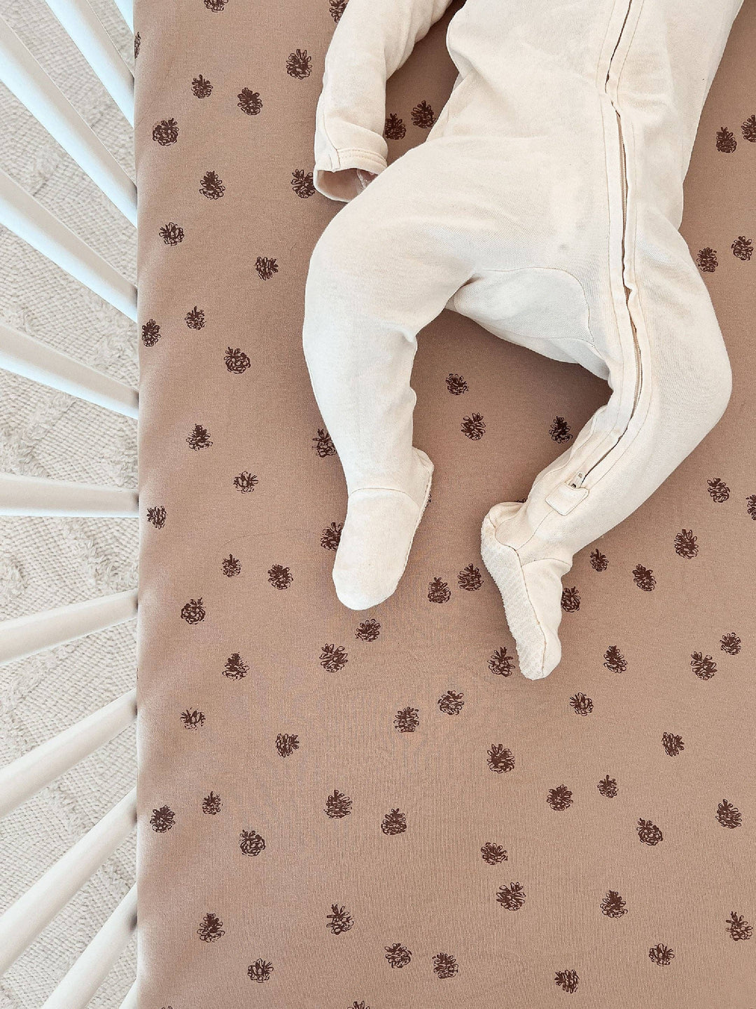 white cotton footie laid overtop of loved baby pinecone oat soft organic crib sheet 