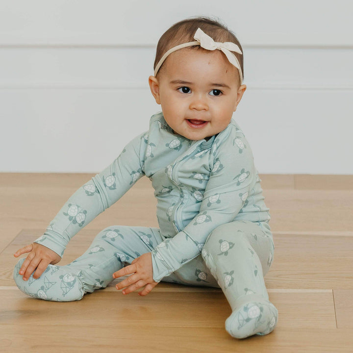 Baby wearing Copper Pearl Wade zip-up footie pajamas sitting on floor, soft bamboo infant sleepwear for everyday comfort