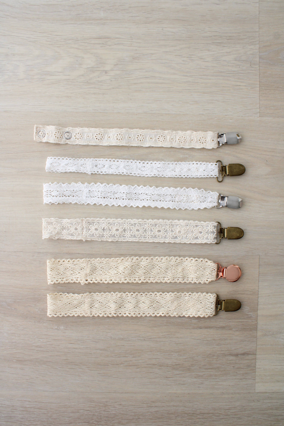 Six neutral paci clips stacked in a row, including the Little Threads Diamond Crochet Collection Pacifier Clip for infants