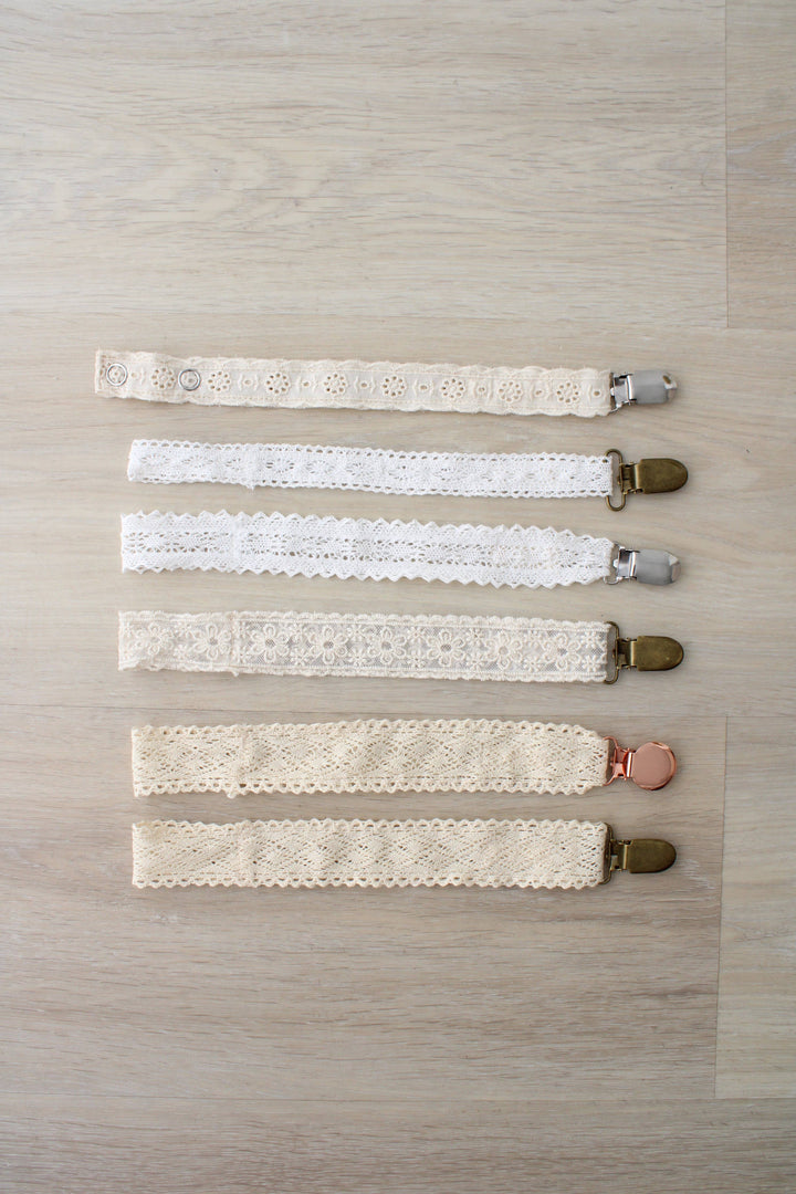 Six neutral paci clips stacked in a row, including the Little Threads Diamond Crochet Collection Pacifier Clip for infants