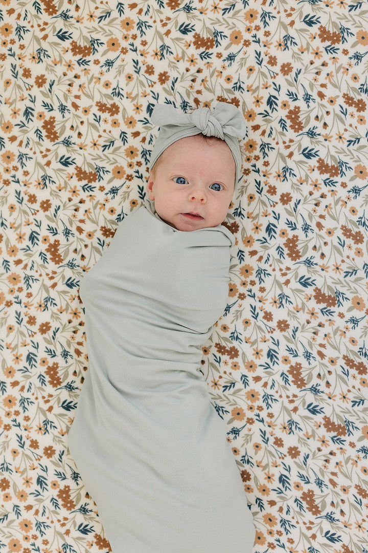Folded on a nursery shelf, the Mebie Baby Sage Bamboo Stretch Swaddle.