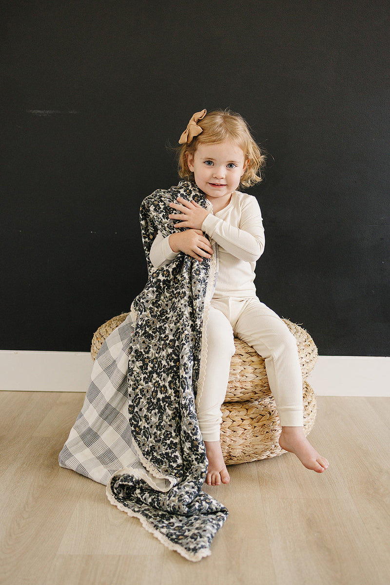 Folded neatly, the Liberty Floral + Coastal Plaid Lace Muslin Quilt from Mebie Baby is a breathable cotton muslin blanket.