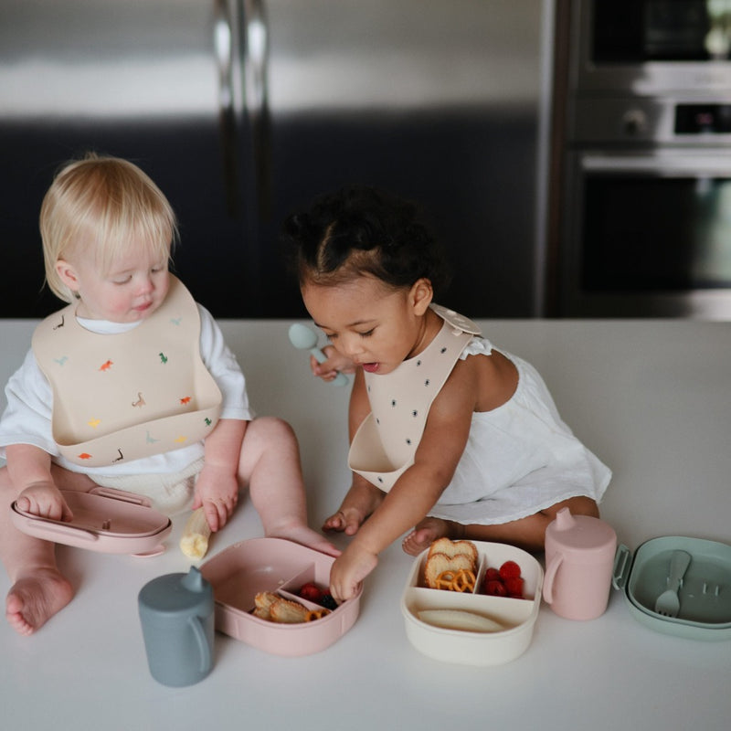 Two Trainer Sippy Cups with Toddlers Eating Out of Lunch Box Two toddlers happily drinking from their trainer sippy cups while enjoying a meal from a lunch box