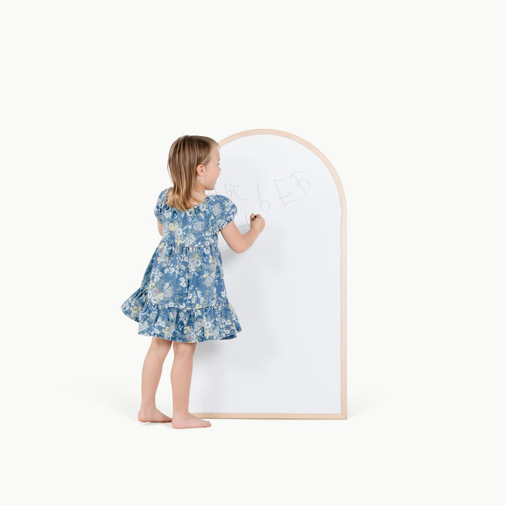 Little girl in a floral dress reaches to draw on the white side of Gathre's magnetic easel