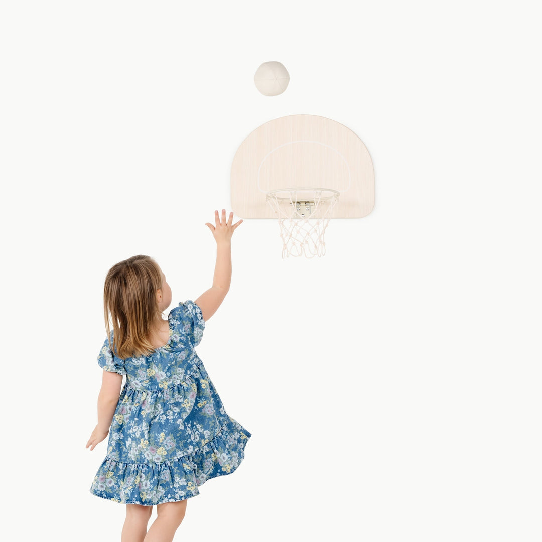 Little girl in a floral dress tosses a ball toward the Gathre Doorway Basketball Hoop
