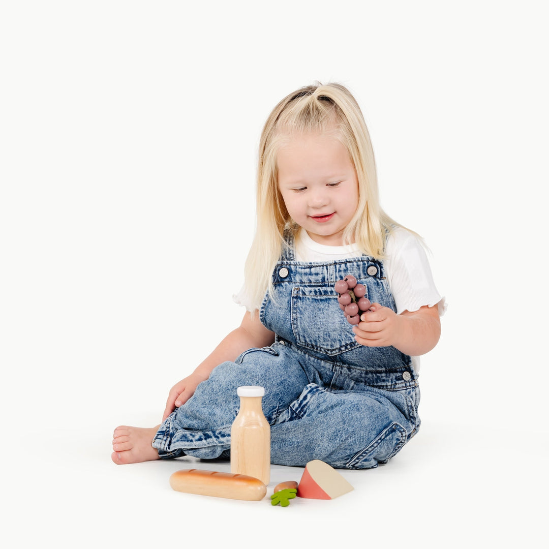 A little girl plays pretend shopping with the Gathre Grocery Set spread out on the floor