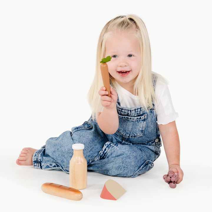 Smiling toddler holds a bunch of play grapes from Gathre's Grocery Set during imaginative play