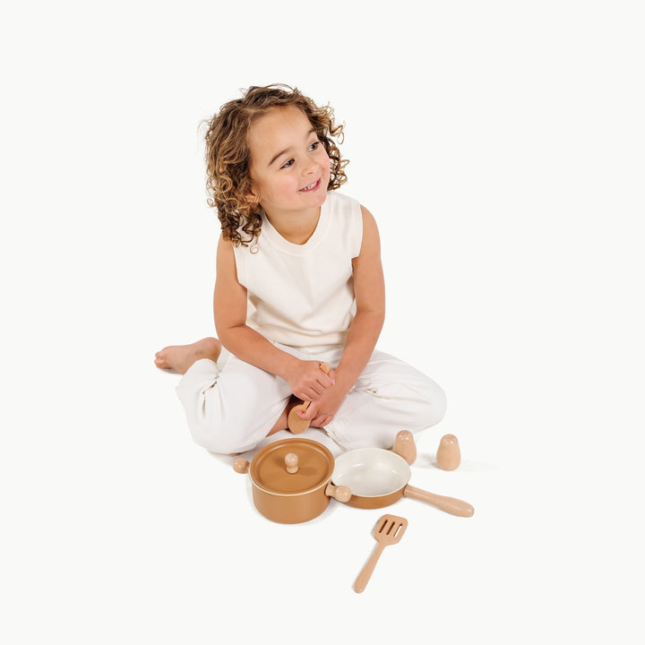 Girl sits with the play stock pot and wooden spoon, enjoying Gathre's pretend kitchen set