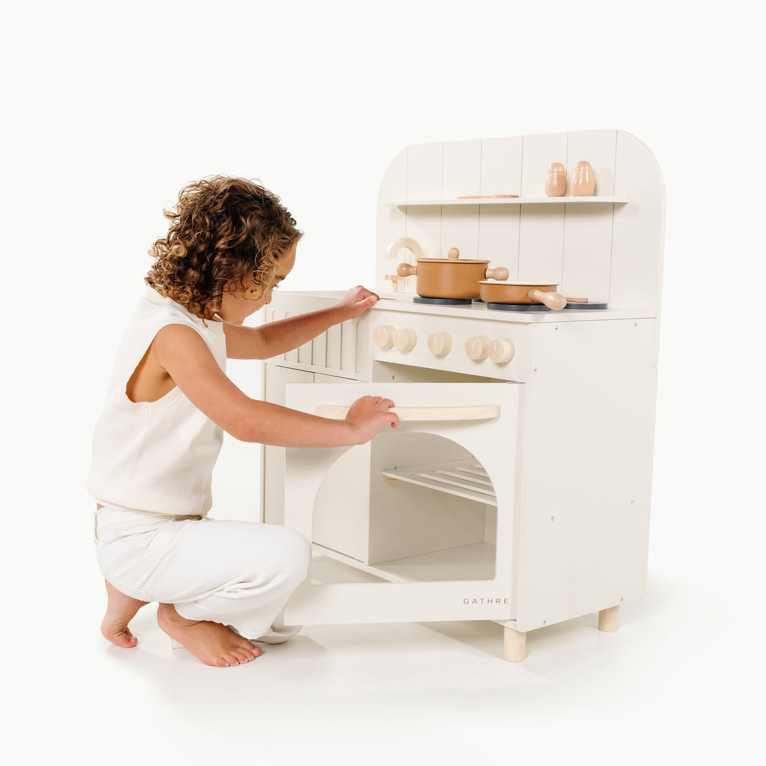 Little girl places a play pot on the stove of her Gathre kitchen during pretend cooking