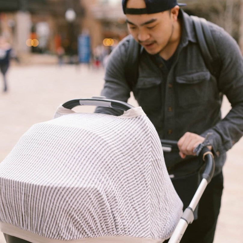 Lifestyle image showing the Little Unicorn Cotton Muslin Car Seat Canopy - Grey Stripe in use, ideal for modern baby car seat protection.