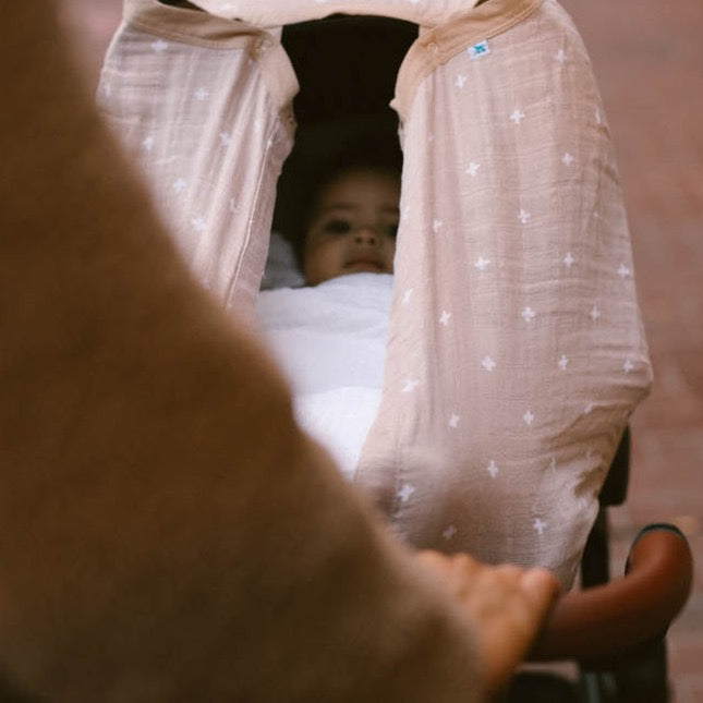 Little Unicorn Cotton Muslin Car Seat Canopy - Taupe Cross pictured on a car seat, providing cozy coverage for everyday outings.