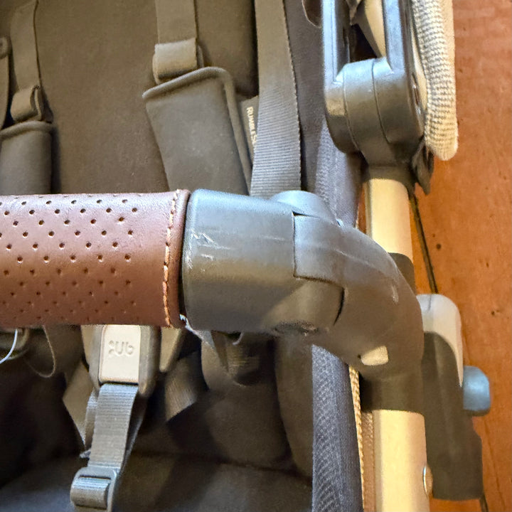 Scuffed bumper bar hub beside chestnut leather on the UPPAbaby RumbleSeat V2+ in Bryce, open box condition detail