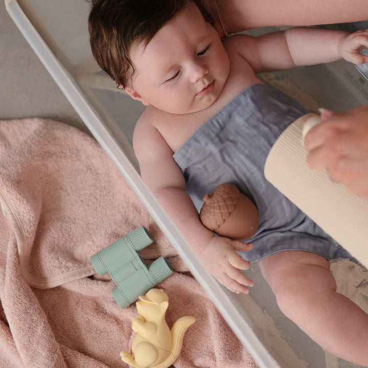 Child playing with Mushie Nature Mold Free Bath Set - toddler holding nature-themed silicone bath toys outdoors