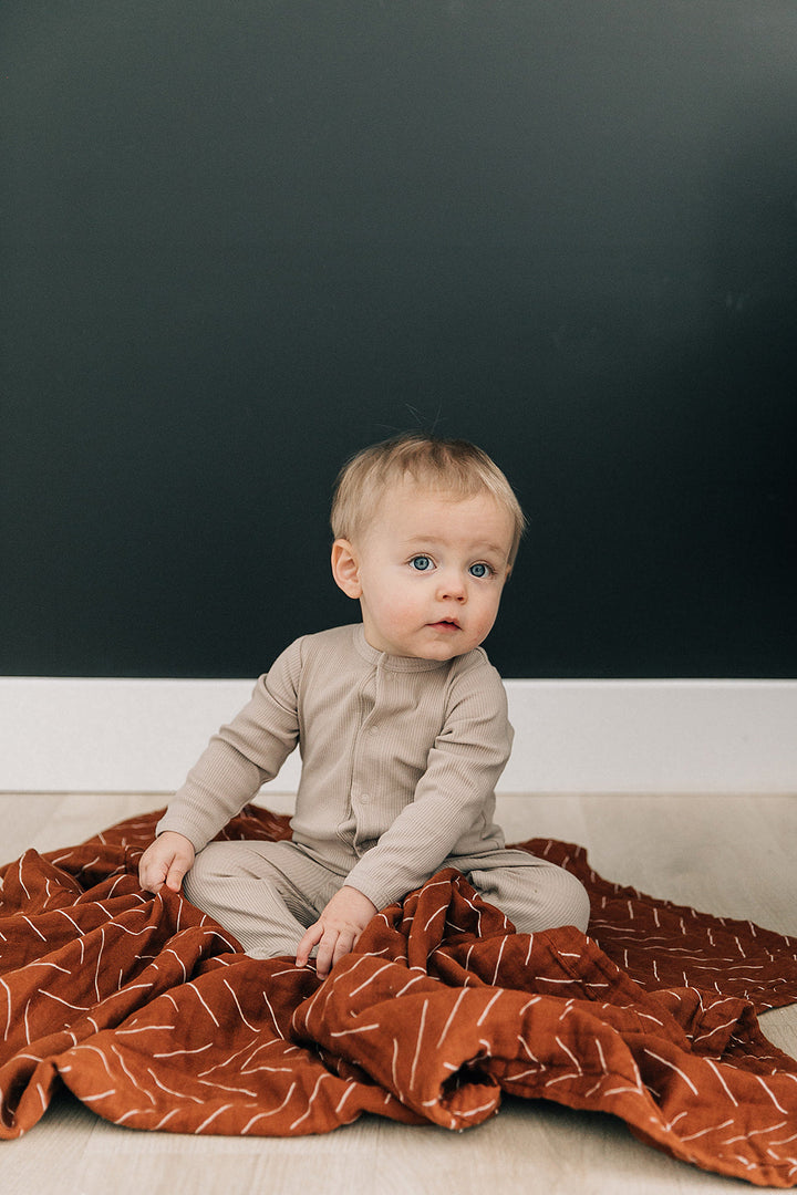 Oatmeal Organic Cotton Ribbed Snap folded next to a stuffed toy, an organic cotton footie pajama for babies.