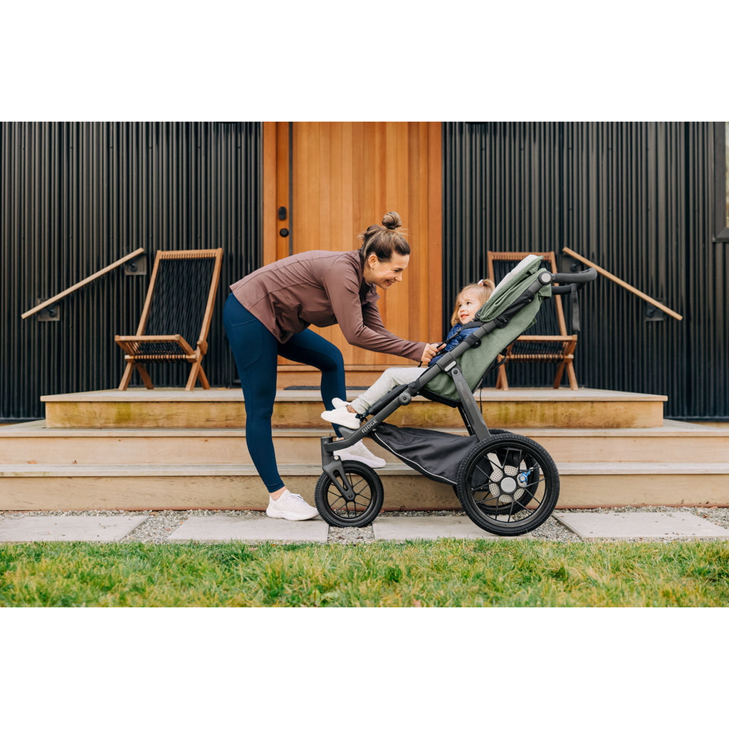 mother buckling child into uppababy ridge jogger stroller