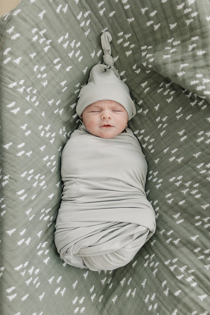 Sage Bamboo Stretch Swaddle draped over a crib rail, a breathable bamboo swaddle blanket for newborns.