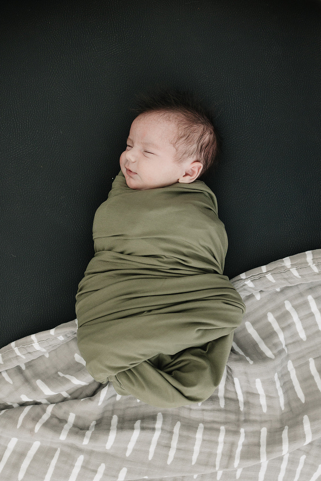 Olive Bamboo Stretch Swaddle draped over a crib rail, a breathable bamboo swaddle blanket for newborns.