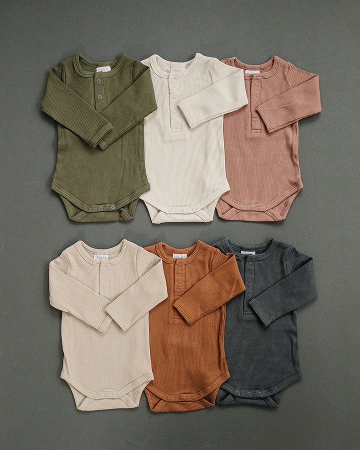 Mebie Baby Oatmeal Organic Snap Long Sleeve Ribbed Bodysuit paired with a knit hat for a nursery flat lay.