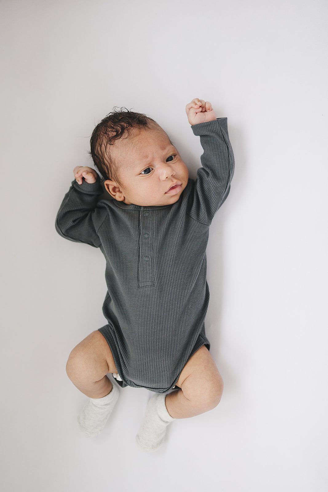 Charcoal Organic Snap Long Sleeve Ribbed Bodysuit folded on a wooden shelf, an organic cotton ribbed baby bodysuit.
