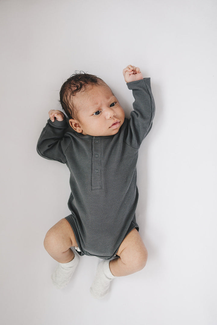 Charcoal Organic Snap Long Sleeve Ribbed Bodysuit folded on a wooden shelf, an organic cotton ribbed baby bodysuit.