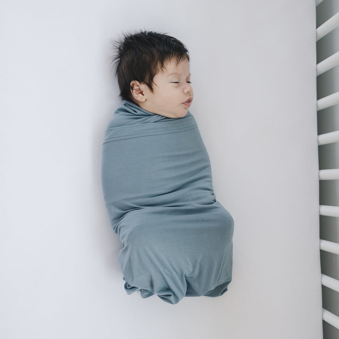 Shown in a flat lay to highlight the fabric, the Mebie Baby Dusty Blue Bamboo Stretch Swaddle.