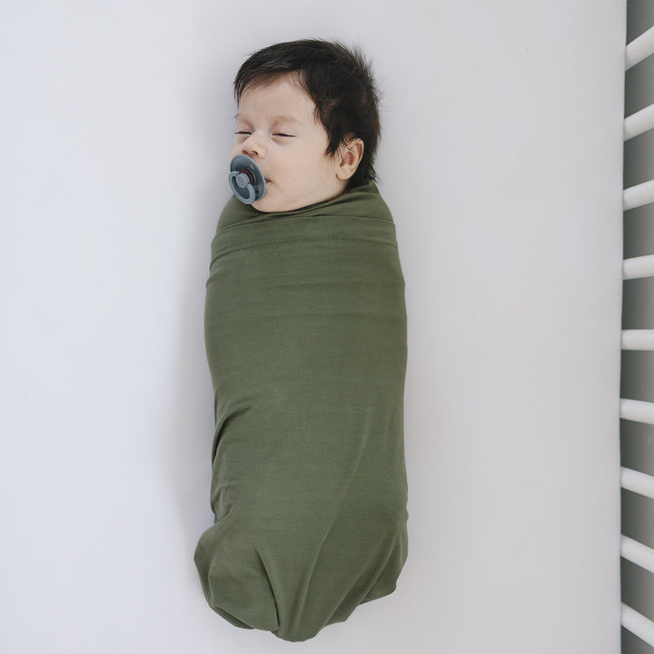 Folded on a nursery shelf, the Mebie Baby Olive Bamboo Stretch Swaddle.