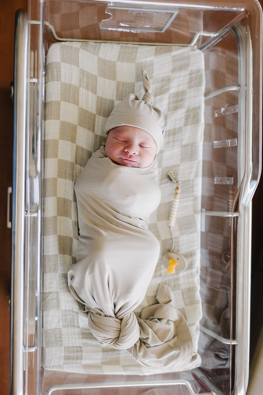 Oatmeal Bamboo Stretch Swaddle draped over a crib rail, a breathable bamboo swaddle blanket for newborns.