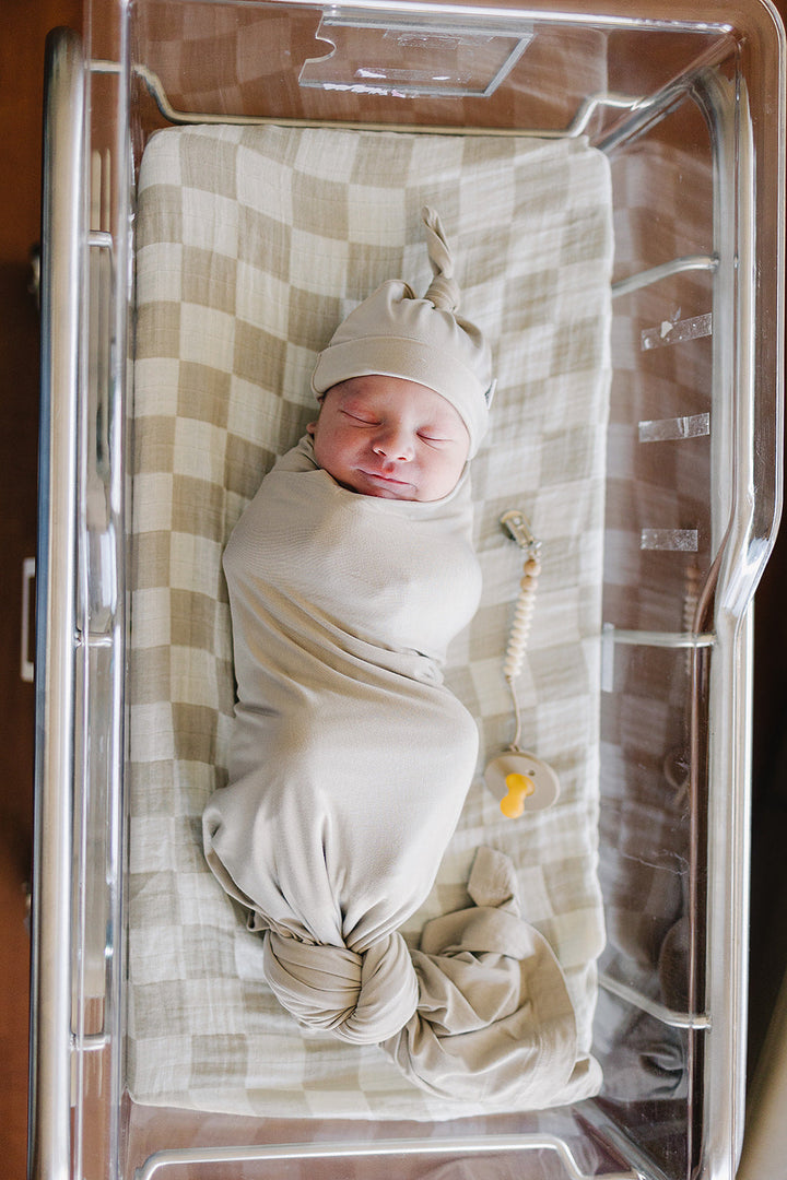 Oatmeal Bamboo Stretch Swaddle draped over a crib rail, a breathable bamboo swaddle blanket for newborns.