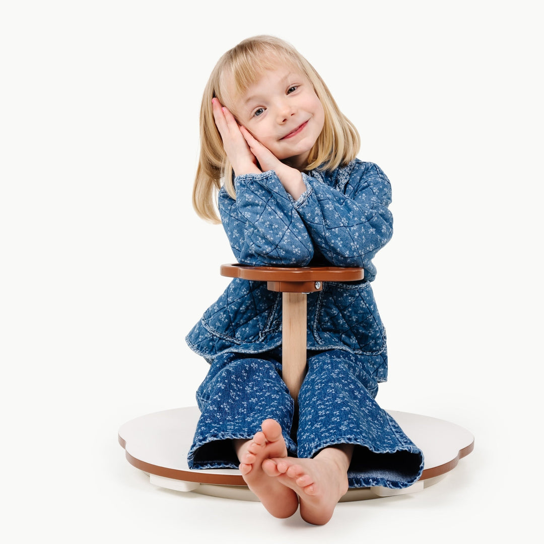 Girl in a blue dress curls up on the spinning seat of Gathre's balance toy