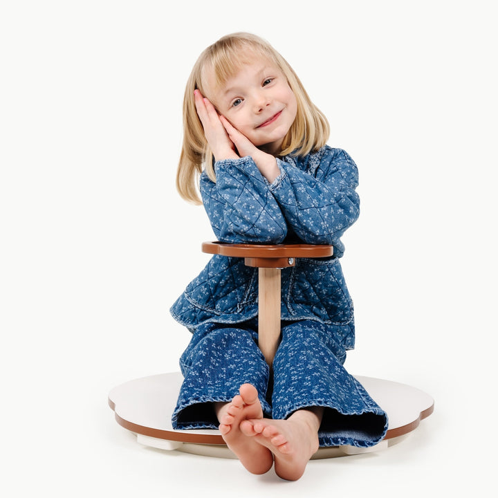Girl in a blue dress curls up on the spinning seat of Gathre's balance toy
