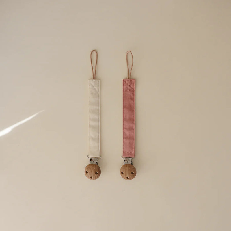 Timeless Dusty Rose and Shifting Sand Mushie Linen Pacifier Clip makes pacifiers easy to keep close and clean.