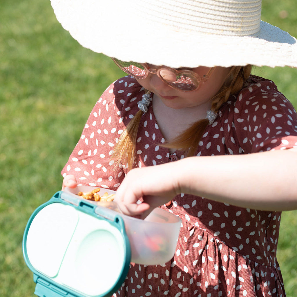 child in sunhat holding snackbox and eating
