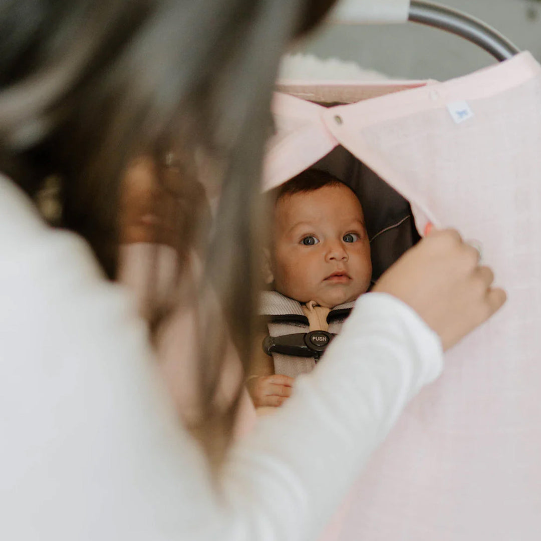Little Unicorn Cotton Muslin Car Seat Canopy - Light Pink displayed on a car seat, offering cozy shade and gentle pastel charm.