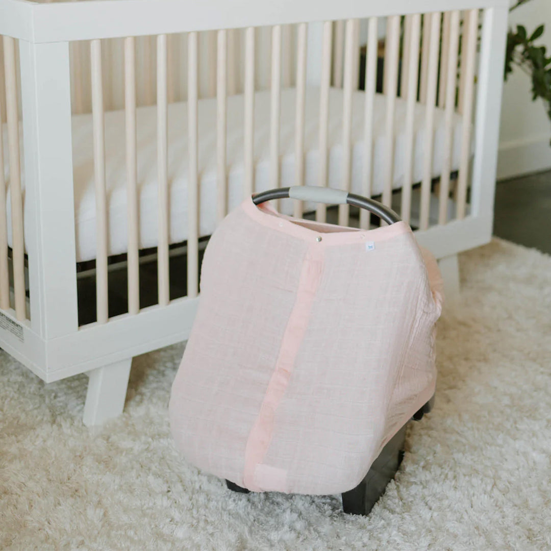 Little Unicorn Cotton Muslin Car Seat Canopy - Light Pink draped over a baby car seat, combining elegance and comfort for travel.