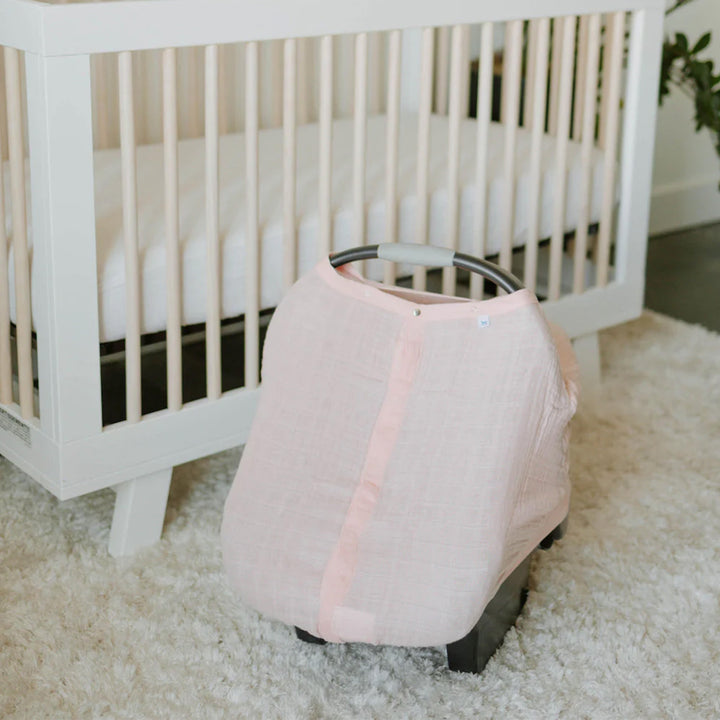 Little Unicorn Cotton Muslin Car Seat Canopy - Light Pink draped over a baby car seat, combining elegance and comfort for travel.