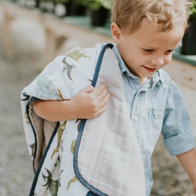 Little Unicorn Original Cotton Muslin Quilt - Dino Friends draped in a nursery, a fun and durable cotton quilt perfect for little adventurers.