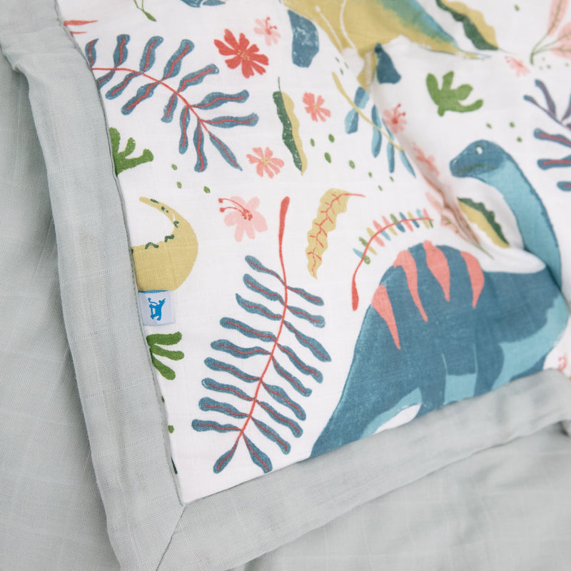 Flat lay of Little Unicorn Cotton Muslin Toddler Comforter - Boho Dino, breathable sleep bags for babies with playful dino print.