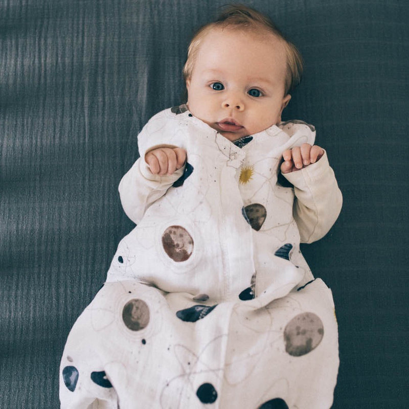 Styled crib image of Little Unicorn Cotton Muslin Sleep Bag - Planetary, breathable sleeping bag baby essential.