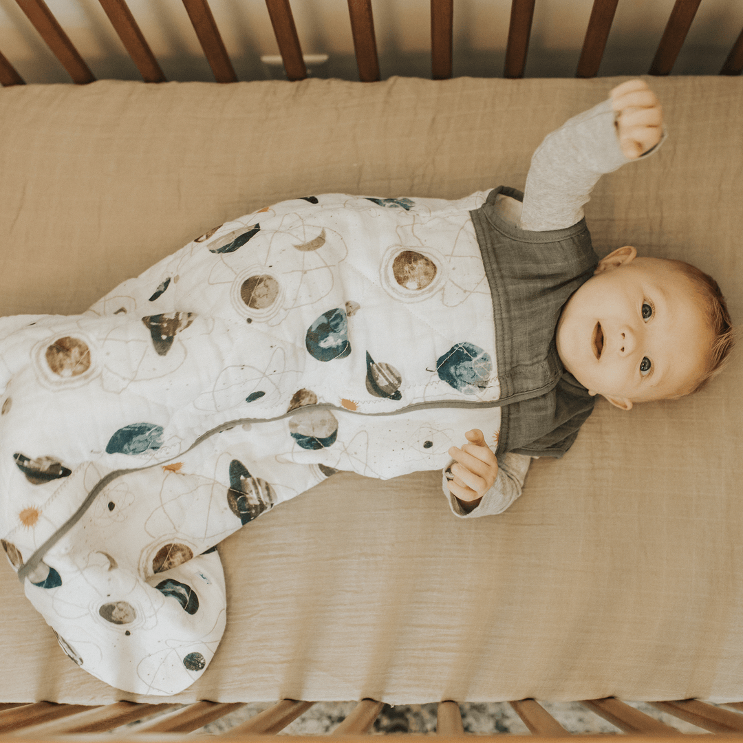 Styled crib shot of Little Unicorn Cotton Muslin Quilted Sleep Bag - Planetary, safe and comfortable sleeping bag baby essential.