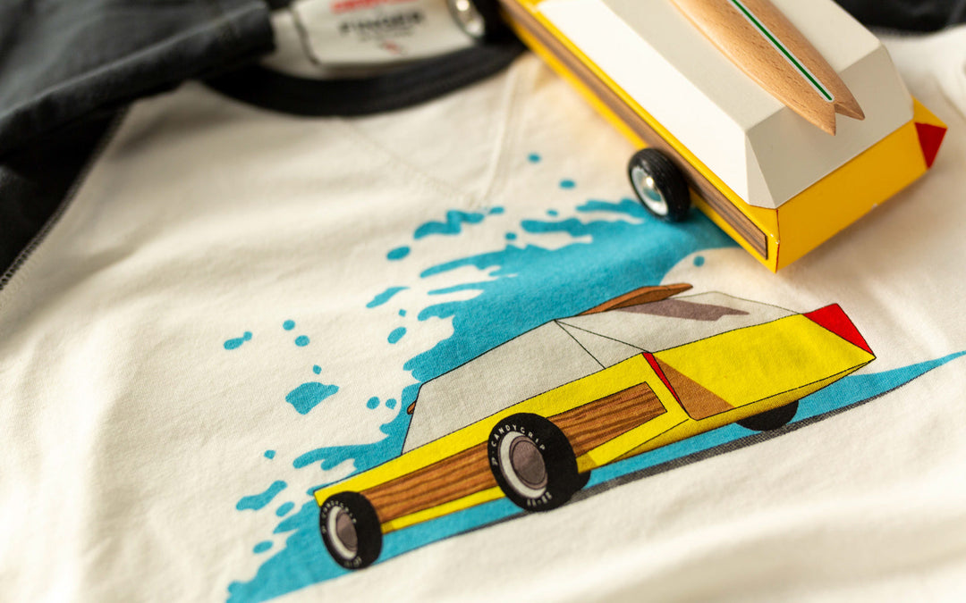 Captured next to a tee in a lifestyle setup, the Plantoys Woodie delivers a stylish wooden car toy aesthetic.