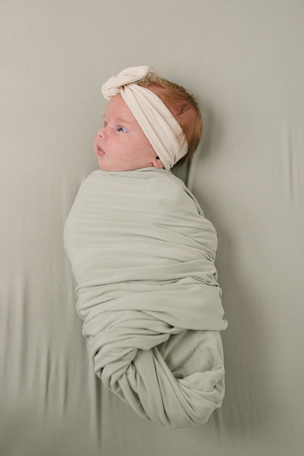 Wrapped around a sleeping newborn, the Sage Bamboo Stretch Swaddle from Mebie Baby.