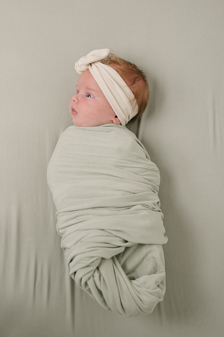 Wrapped around a sleeping newborn, the Sage Bamboo Stretch Swaddle from Mebie Baby.