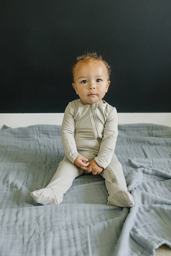 Shop baby footie pajamas at Mebie Baby, the Oatmeal Bamboo Footed Zipper styled for a nursery flat lay.